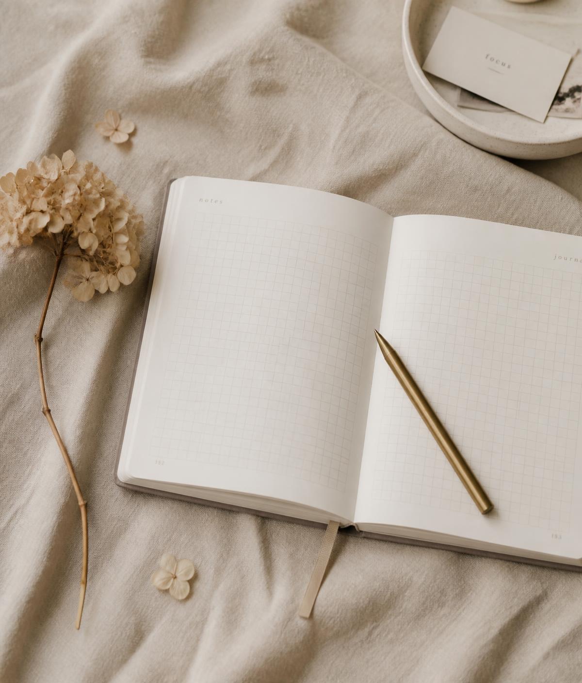 An open Inklier journal with grid pages and a gold pen